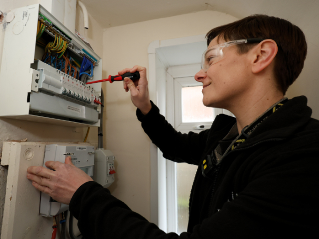 Female electrician installing a new a fuse box in a council home