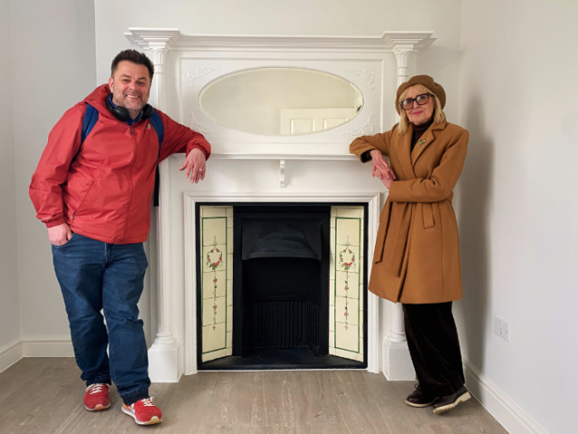 Image shows Cllr Gill Williams and Cllr Paul Nann, standing at a beautiful ornate fireplace and smiling.