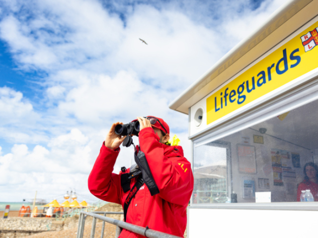 Lifeguard in red jacket looking through binoculars.