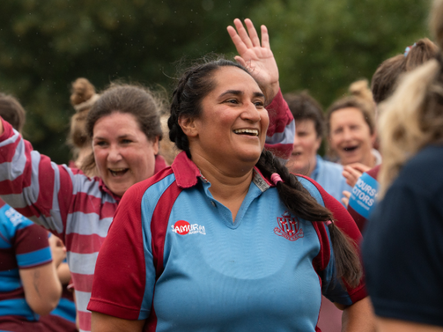 A women in a blue rugby shirt is smiling in front of other women cheering