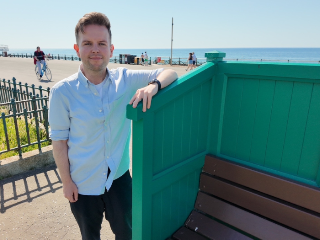 Councillor David McGregor by one of the newly restored Cucumber benches on Hove seafront