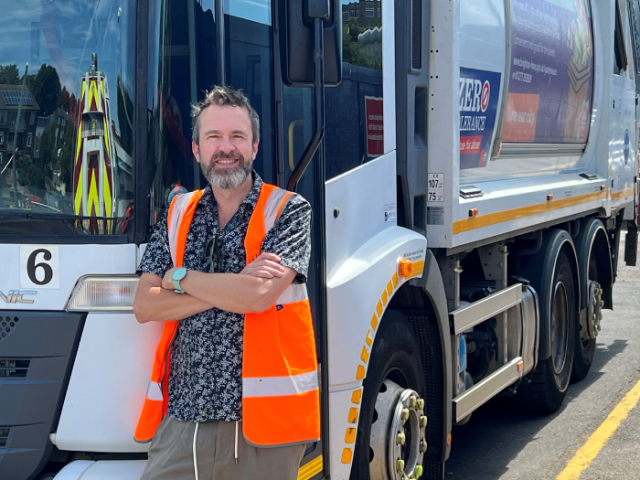 Man in an orange hi-viz vest stood in front of a waste truck.