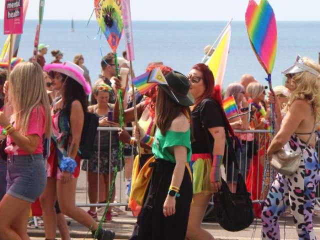 People dressed in colourful clothes marching in the Pride parade with the sea in the background. 