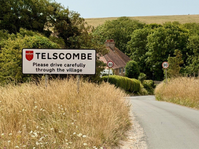 Road sign saying Telscombe with view of village in the background