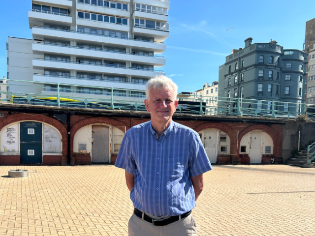 Councillor in a blue shirt and light trousers soon in front of seafront arches.