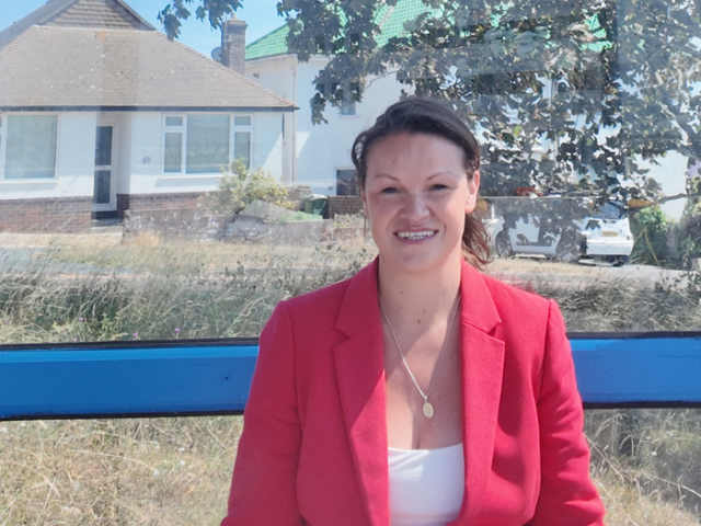 Council leader Bella Sankey in a red jacket with houses in the background.