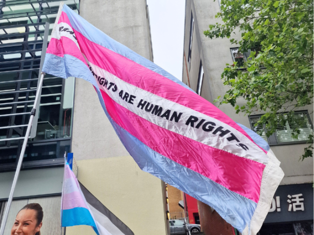 Large Trans flag flying with words Trans rights are human rights embroidered in the centre.