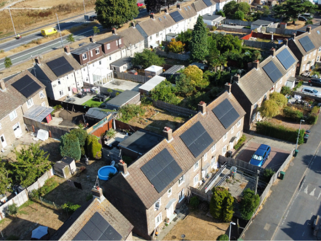 The image shows a drone photo of Newick road in Moulsecoomb, with roofs covered in solar panels.