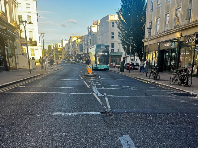 Road surface with defects and a double-decker bus in the background.
