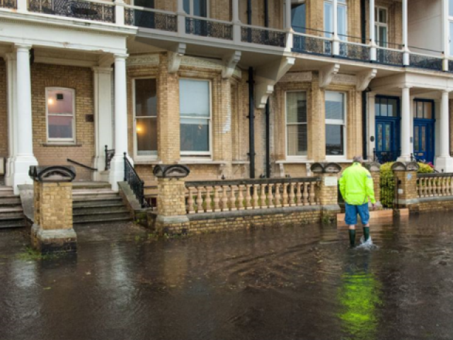 Person walking along a flooded street in Brighton and Hove in wellington boots with water above the ankles, because the pavement in front of terraced houses is submerged