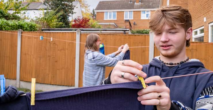 Teenager hanging washing on line in a garden. An adult also hangs washing on the line in the background