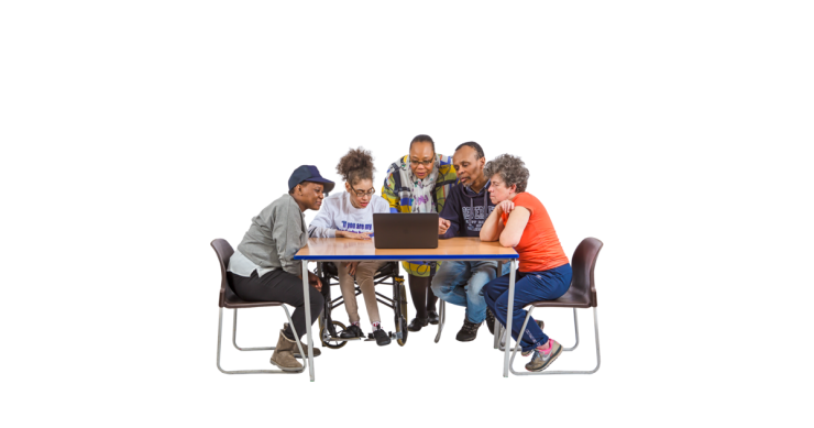Group of people sat around a table looking at a laptop.
