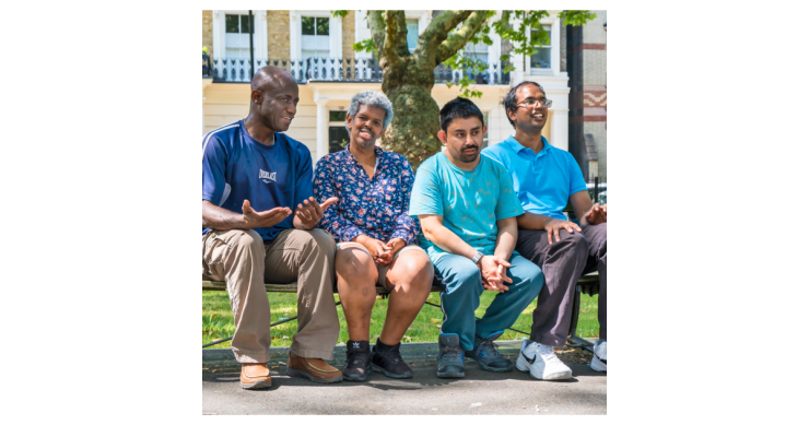 Four people sitting on a bench in the park.