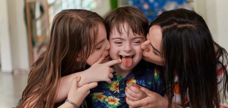 A woman and young girl kissing a Down Syndrome young boy