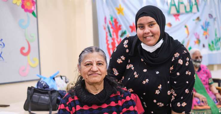 2 people smiling at the camera, 1 is sitting down the other is standing behind