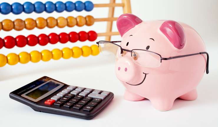 A china piggybank wearing glasses, next to a calculator with an abacus in the background