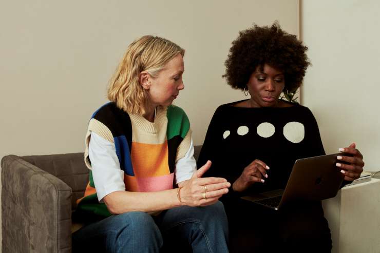 2 people sat on a sofa having a conversation and looking at a laptop