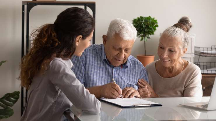 A group of 3 people sitting at a table, one of them is writing on a clipboard