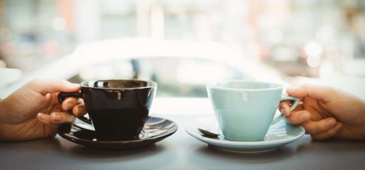 2 hands holding 2 cups on saucers on a table