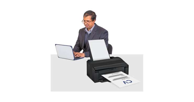 Person at a desk typing on a laptop and printing out their CV.