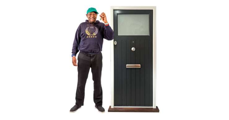 Person proudly holding a key in front of a house front door.