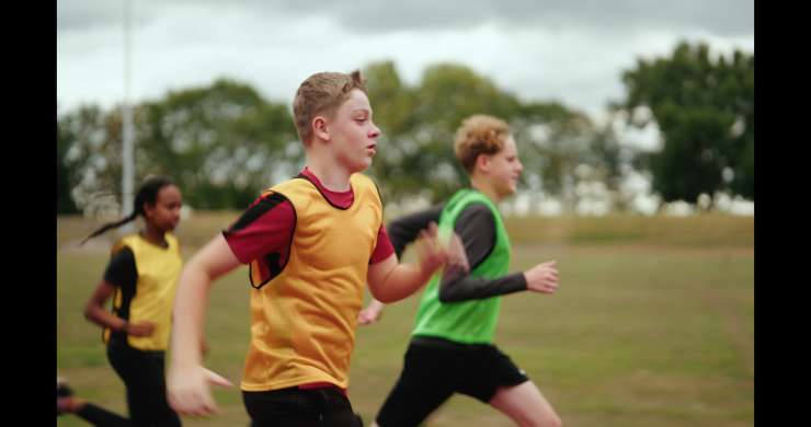 Young people in a sports field competitively running. 