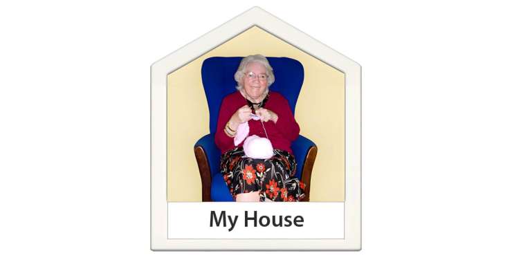 Older person sitting in a chair knitting. 
