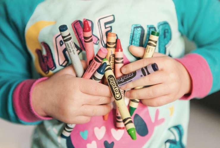 Toddler holding lots of different coloured crayons.