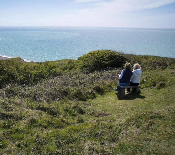 2 people overlooking the sea on a bench in the countryside.