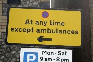 Photograph of a sign saying no stopping at any time except ambulances, the sign is bright yellow and has a symbol with a blue circle with a red x through it
