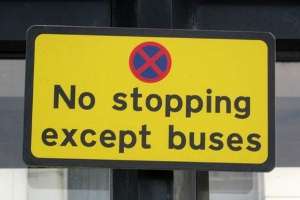 Photograph of a sign saying no stopping except buses, the sign is bright yellow and has a symbol with a blue circle with a red x through it