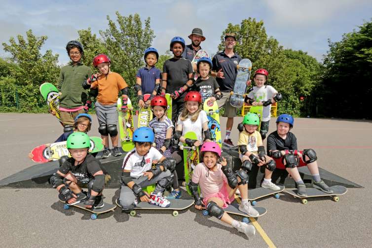 A group of children pose for a photo with their safety helmets and skateboards after a HAF skateboarding workshop